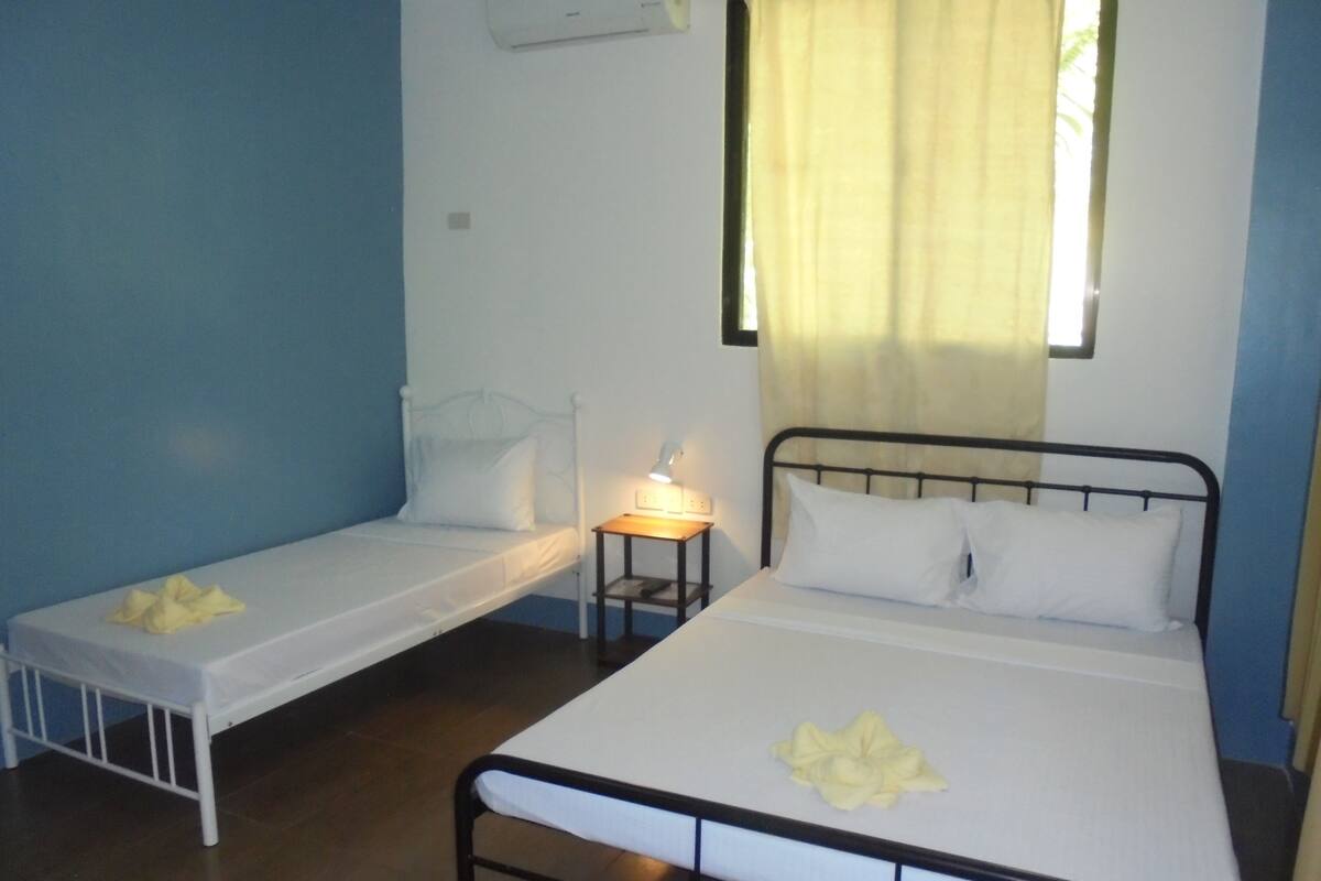 A room with two single beds, a small table with a lamp, and a window with curtains.