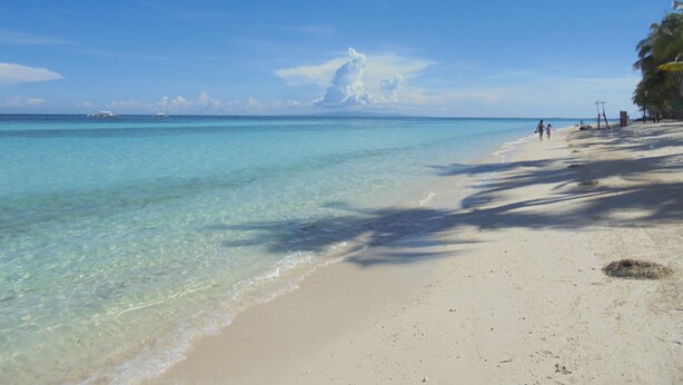 A beach with clear turquoise water, a sandy shore, and a few people walking. - Maya Playa (Panglao)