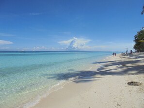 A beach with clear turquoise water, a sandy shore, and a few people walking. - Maya Playa (Panglao)
