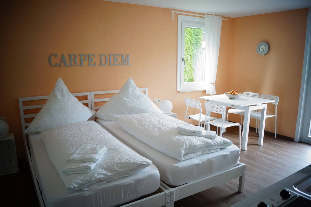 A room with two beds, a table with chairs, a clock, and a window with curtains.