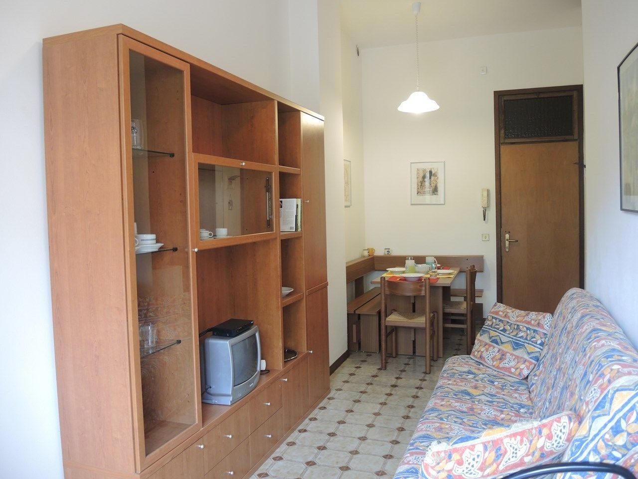 A compact living space with a wooden cabinet, a patterned sofa, a dining table, and a small television.
