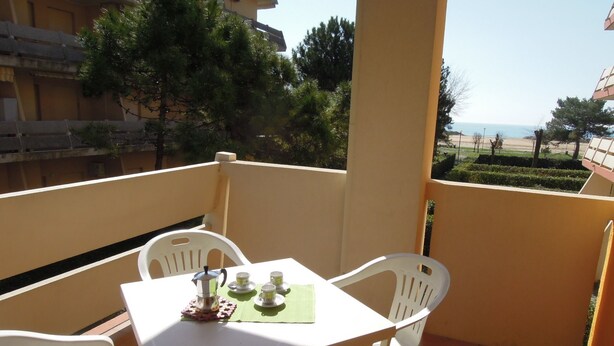 A balcony with a table set for two, chairs, and a view of the sea.