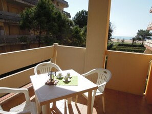 A balcony with a table set for two, chairs, and a view of the sea. - Condominio Carina (San Michele al Tagliamento)