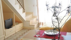 A dining area with a table set for two, a television in the background, and a staircase leading to another level.