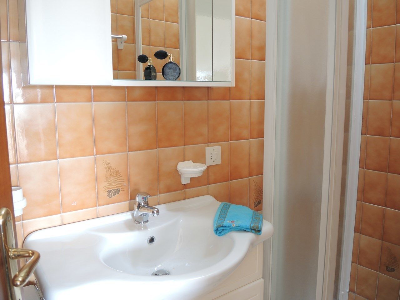 A bathroom with a white sink, a mirror, and orange-tiled walls.