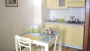 A compact kitchen with yellow cabinets, a sink, and a stove. There is a dining table with chairs and a framed picture on the wall.