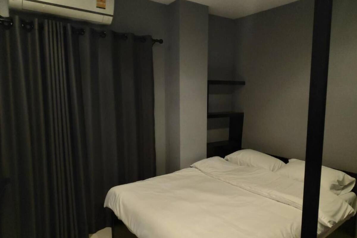 A single bed with white bedding, a dark curtain, and a wall-mounted air conditioning unit.