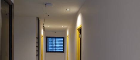 Un pasillo con piso pulido, iluminación empotrada y una ventana con persianas.