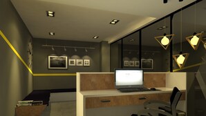 A modern office space with a desk, computer, and chair. There are framed pictures on the wall and a bookshelf.
