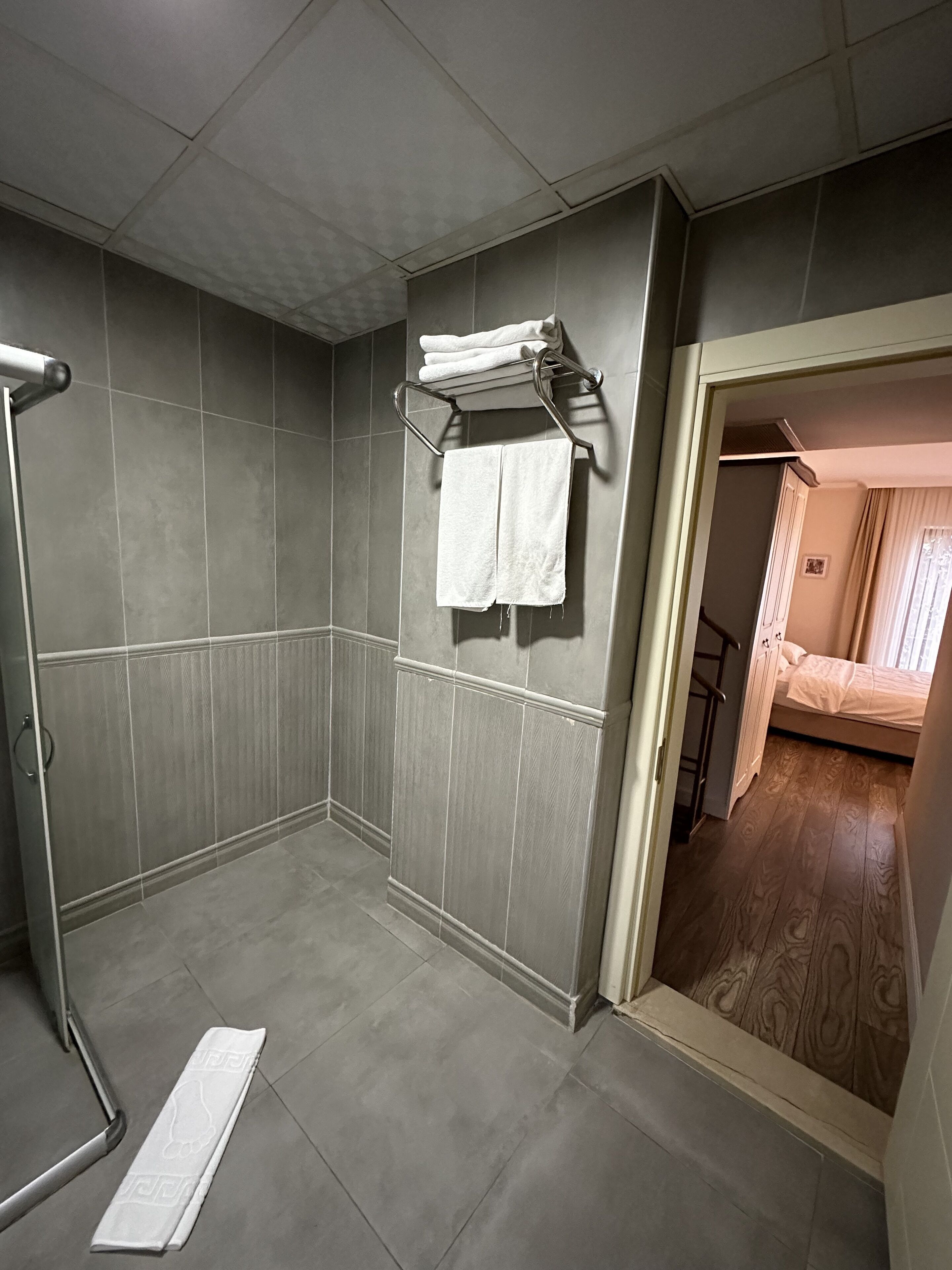 A bathroom with grey tiles, a shower area, and a towel rack with two towels.