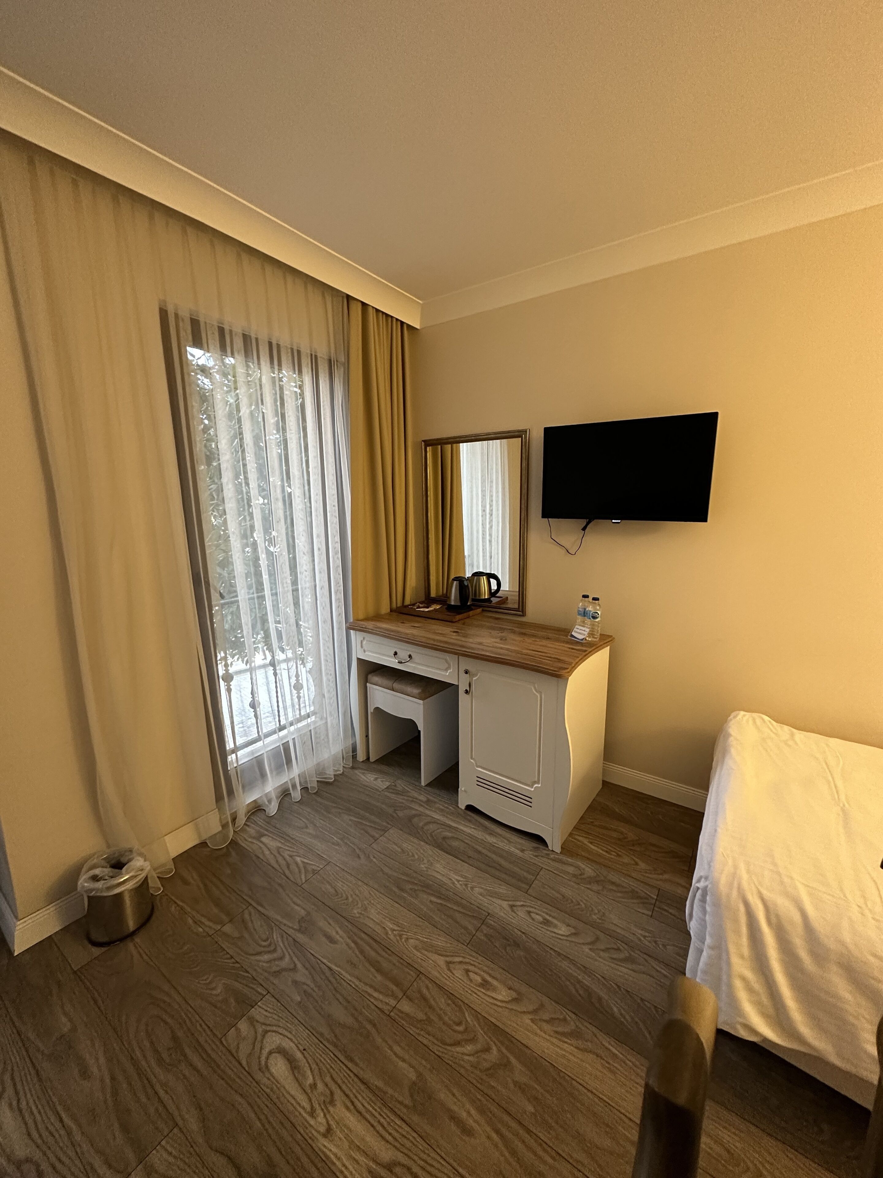 Una habitación de hotel con escritorio de madera, cama, televisor montado en la pared y ventana con cortinas.