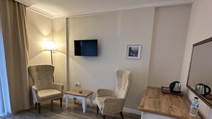 A hotel room with a wooden floor, two armchairs, a small table, a sofa, a TV mounted on the wall, and a bedside table with a kettle and water bottle. - Biga Casa Grande Otel (Biga)