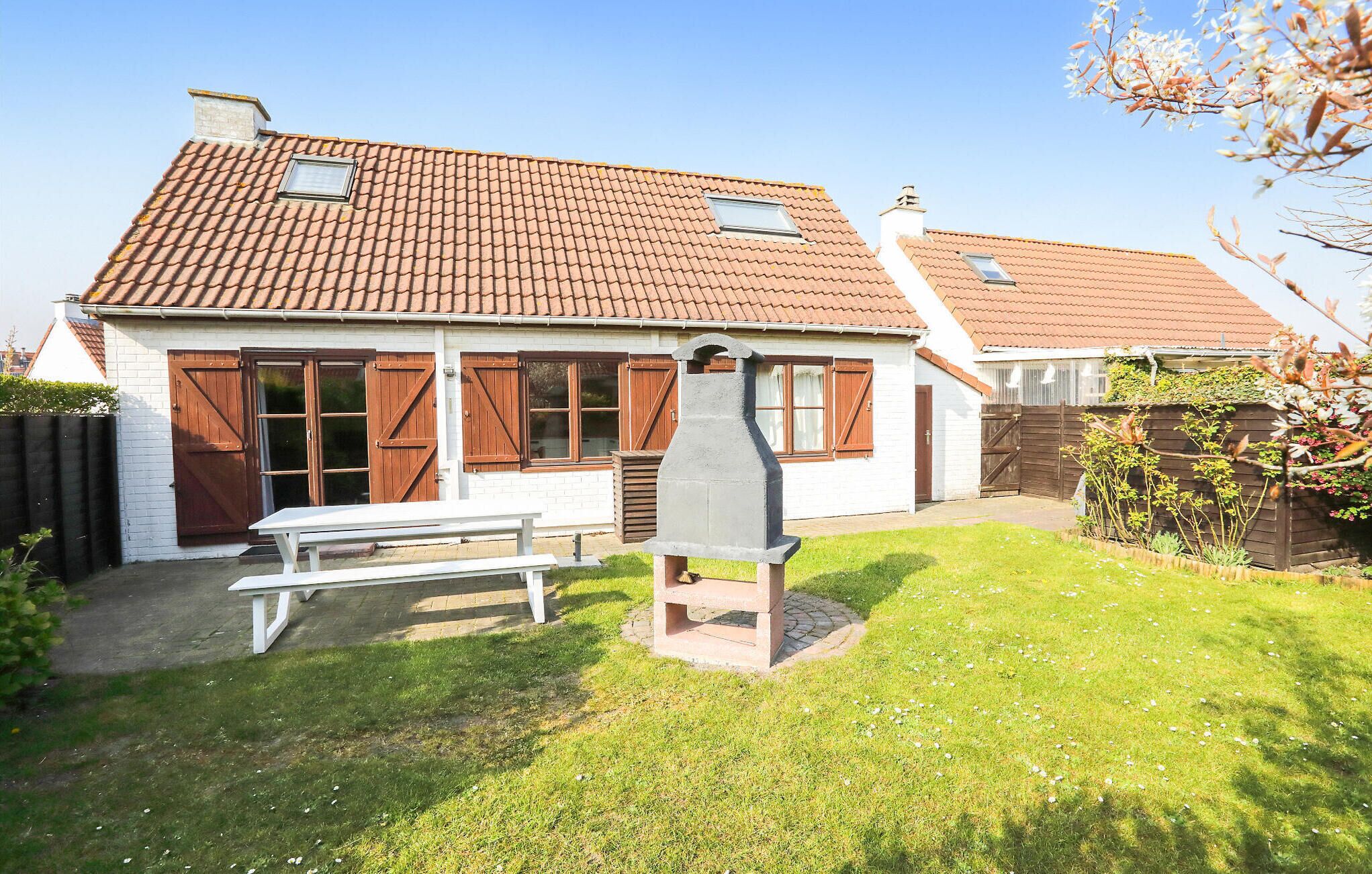 A house with a tiled roof, a chimney, a wooden fence, and a picnic table.