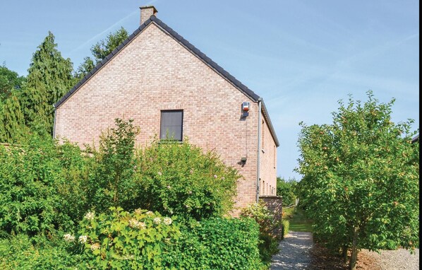 Een gebouw van baksteen met een klein raam en een deur, omgeven door weelderige begroeiing en bomen.