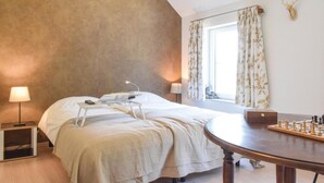 Hotellihuone, jossa on suuri sänky, yöpöydällä lamput, kirjoituspöytä lampun kanssa, ikkuna verhoilla ja shakkilauta.