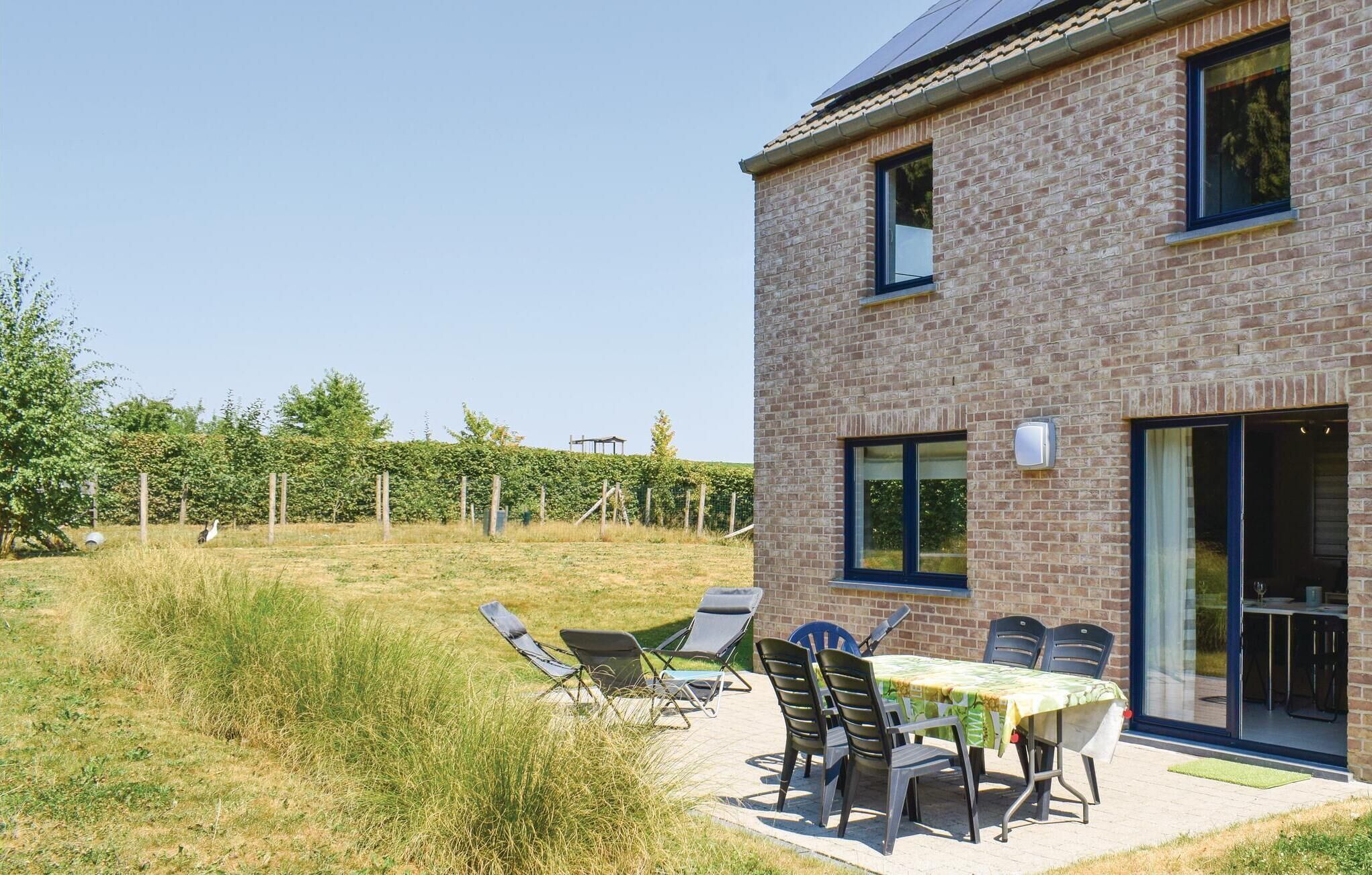 Een modern bakstenen huis met een terras, een tafel en stoelen, een grote schuifpui en een uitzicht op een wijngaard op de achtergrond.