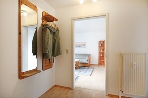 A hallway with a coat rack, a radiator, and a view into a living room with a sofa and a bookshelf.