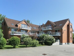 Ein mehrgeschossiges Wohngebäude mit Balkonen, einem gepflasterten Innenhof und umliegender Bepflanzung.