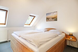 Un dormitorio con una cama de madera, dos tragaluces, un radiador y un cuadro en la pared.