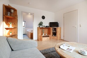 Una sala de estar acogedora con un sofá gris, armarios de madera, un televisor de pantalla plana y una mesita con una revista y una taza.