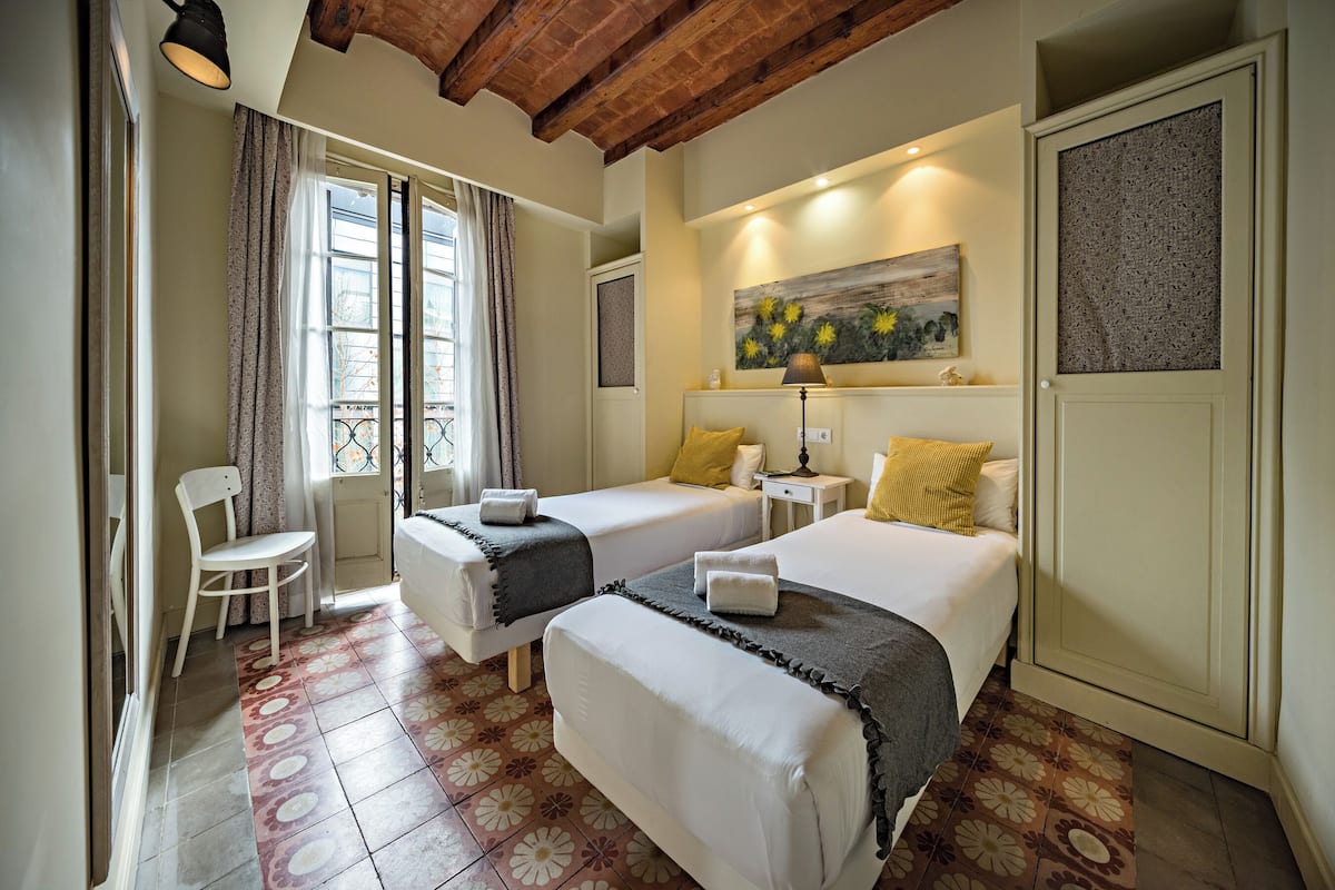 Une chambre d’hôtel avec deux lits, une chaise, un tableau et une fenêtre avec des rideaux.