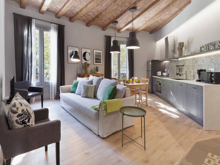 Una sala de estar moderna con un sofá, una mesa de centro y un comedor con una mesa y sillas. Hay una zona de cocina con un refrigerador y una cafetera.