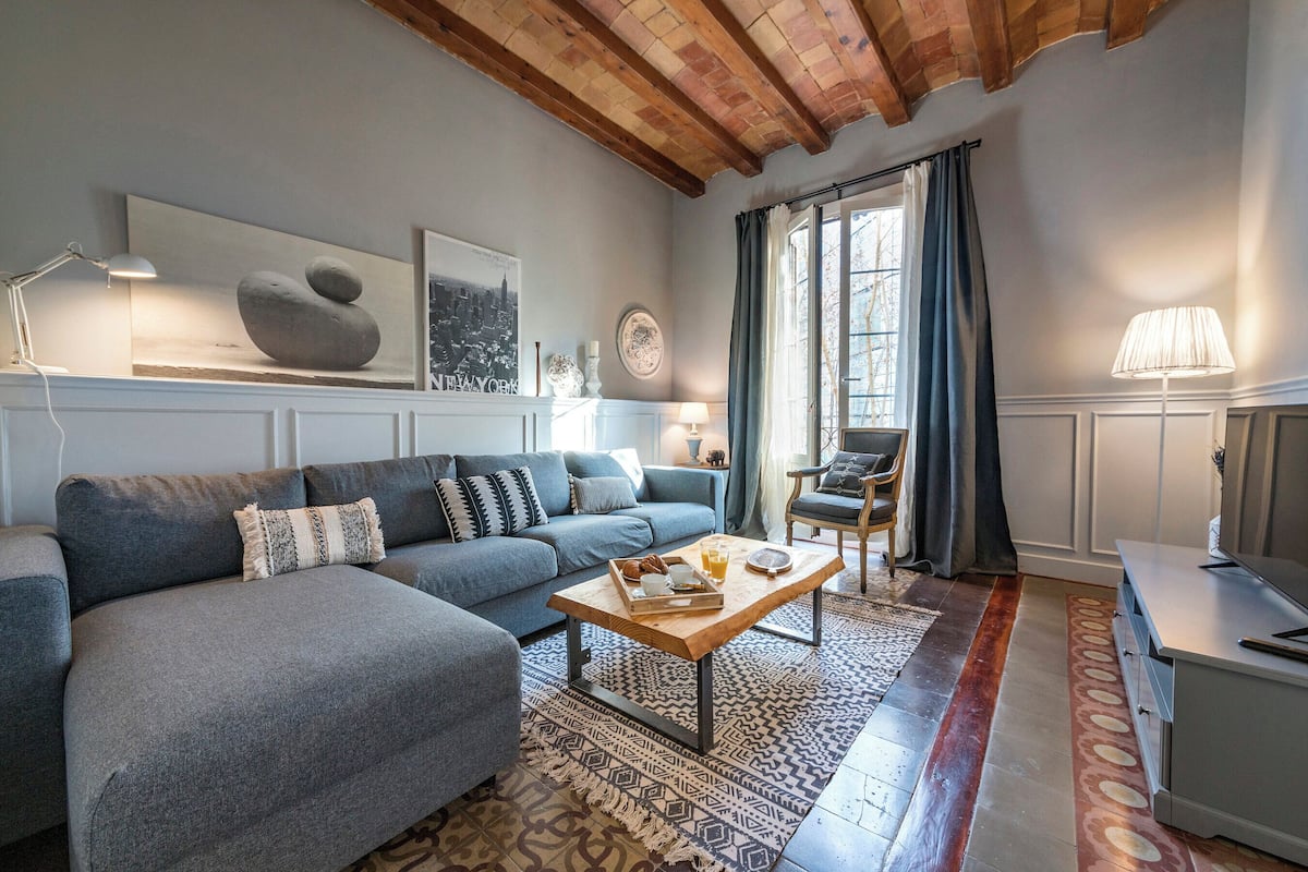 Un salon moderne avec un canapé gris, une table basse en bois et un tapis à motifs.