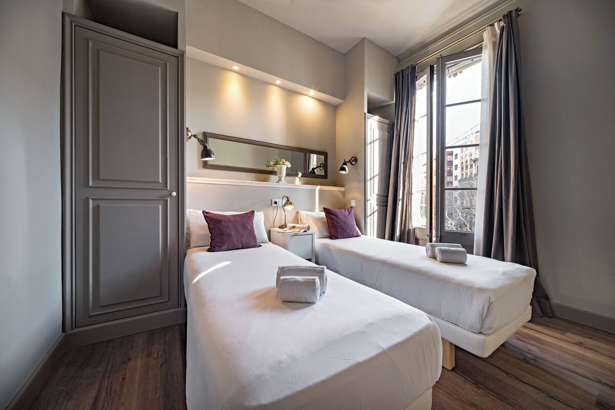 Une chambre d’hôtel avec deux lits, une table de chevet, un miroir et une fenêtre avec des rideaux.