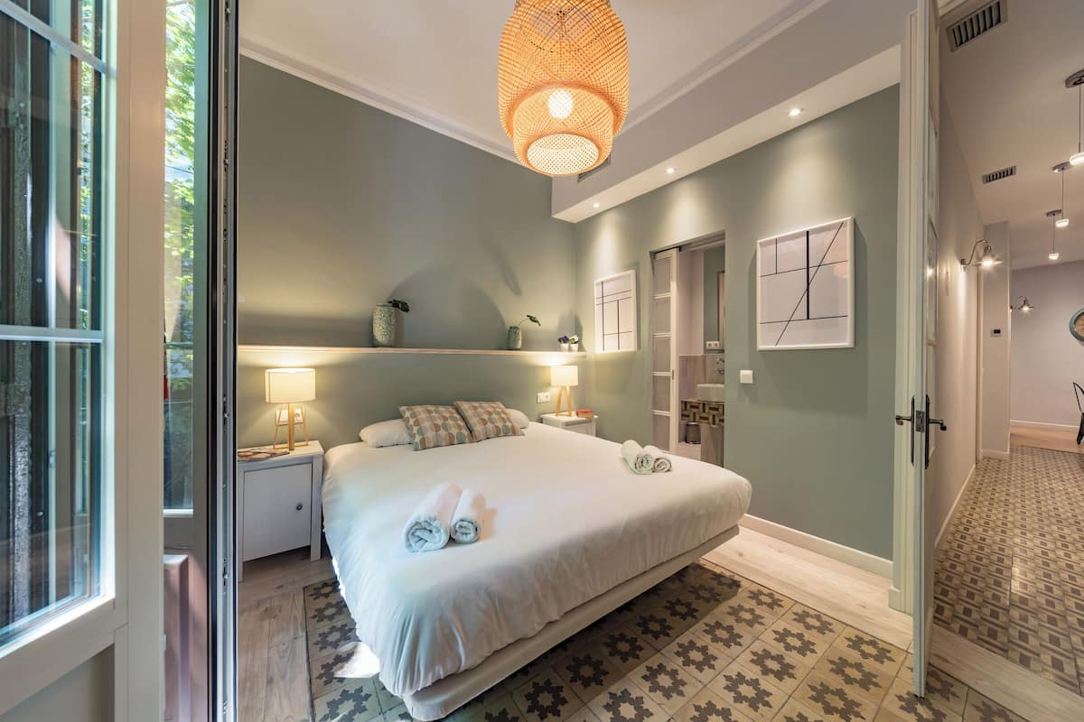 Une chambre avec un grand lit, des lampes de chevet, une étagère décorative fixée au mur et un tapis à motifs.