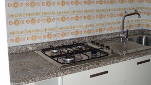 A kitchen with a gas stove, stainless steel sink, white cabinets, and patterned tile backsplash. - Ville Schiera (San Michele al Tagliamento)