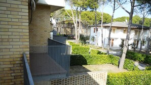 A residential building with a brick facade, a metal balcony, and a well-maintained garden with hedges and trees. - Ville Schiera (San Michele al Tagliamento)