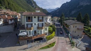 A multi-story building with balconies, a paved street, and a mountainous backdrop. - Hotel Ristorante Sporting Club (Ballabio)