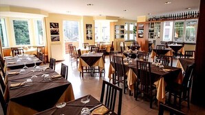 A restaurant with multiple tables and chairs, large windows, and a wine rack on the right wall. - Hotel Ristorante Sporting Club (Ballabio)
