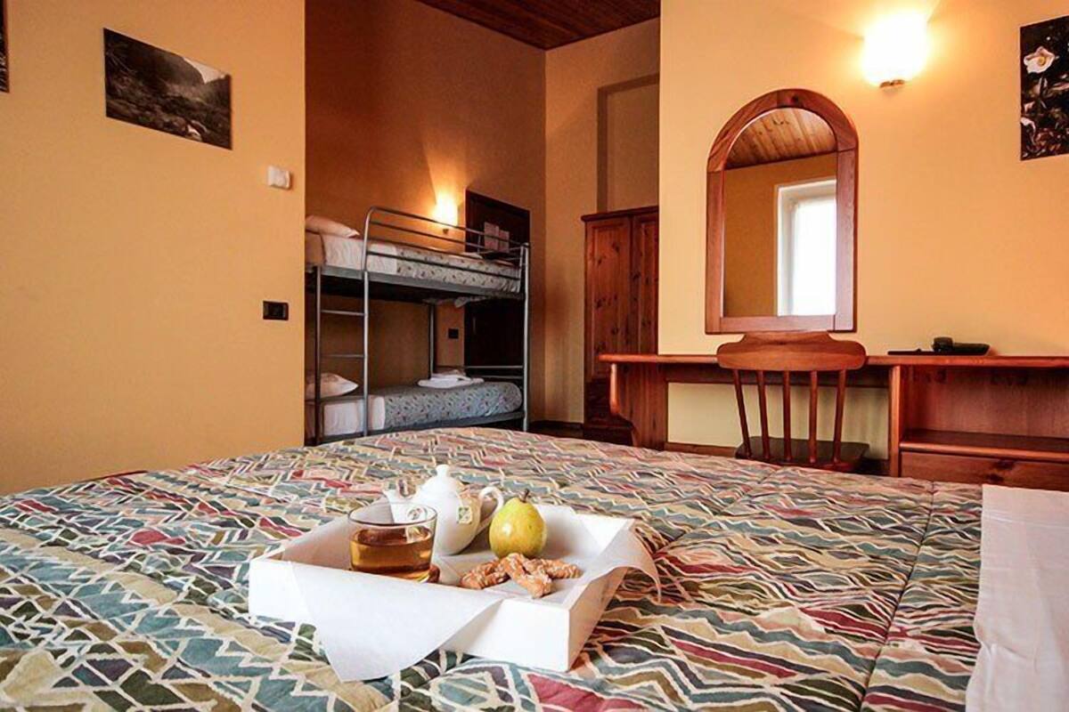 A room with a bunk bed, a desk, a mirror, and a breakfast tray with tea, a pear, and pastries.