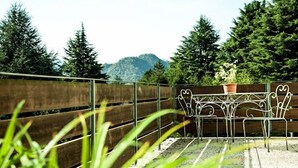 A patio with metal chairs and a table, surrounded by a wooden fence and tall trees. - Hotel Ristorante Sporting Club (Ballabio)