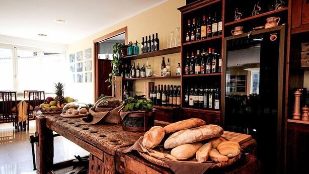 A bar area with a rustic wooden counter, shelves of wine bottles, and a variety of bread and fruits. - Hotel Ristorante Sporting Club (Ballabio)