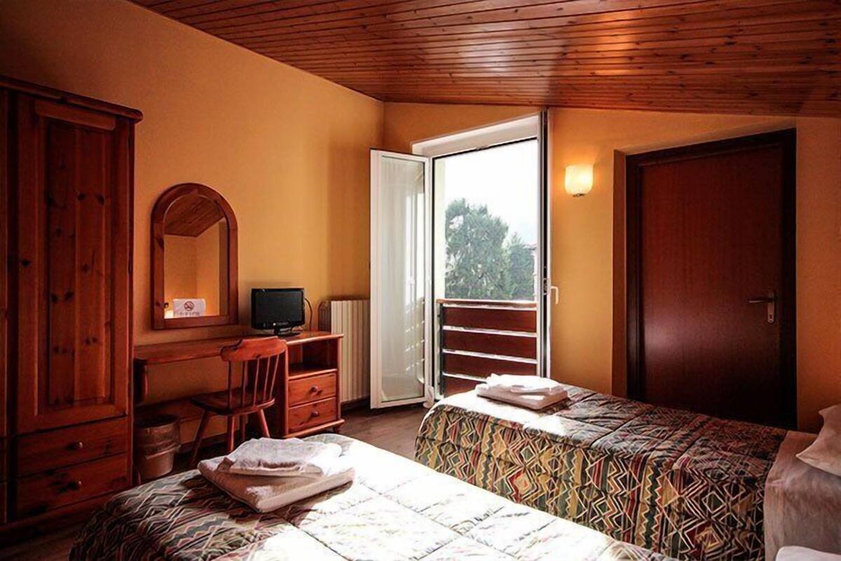 A bedroom with two beds, a desk, a chair, a wardrobe, and a sliding glass door to the outside.