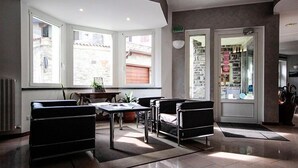 A modern hotel lobby with a large window, a reception desk, and leather armchairs. - Hotel Ristorante Sporting Club (Ballabio)