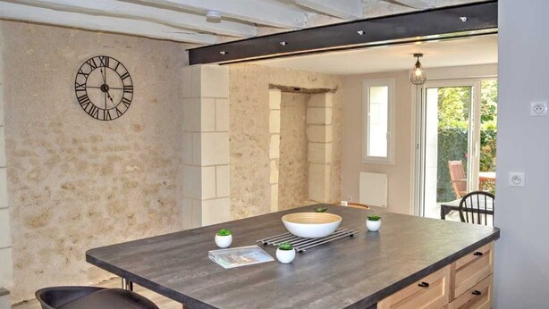 A modern kitchen with a central island, bar stools, a clock, and a view of the outdoors.