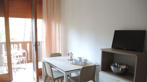 Un coin repas comprenant une table, des chaises, un téléviseur posé sur une étagère et une vue sur l’extérieur.