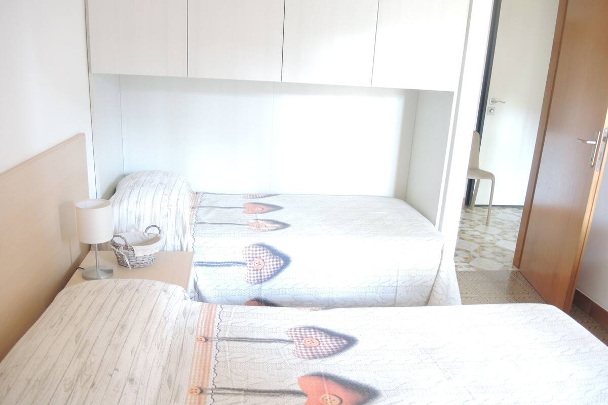 Une chambre avec deux lits, une table de chevet avec une lampe, un panier en osier et une chaise.