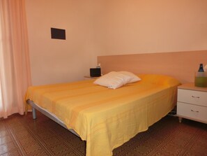 A single bed with a yellow bedspread, a white pillow, a nightstand with a lamp, and a bottle of water on the side table.