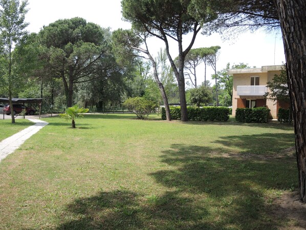 Une zone herbeuse avec des arbres et un bâtiment doté d’un balcon.