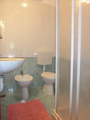 A bathroom with a sink, bidet, toilet, and a shower area.