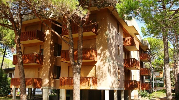 Un immeuble à plusieurs étages, doté de balcons et entouré d’arbres.