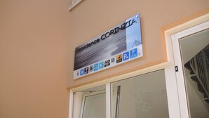 Une enseigne indiquant « Résidence Corinzia », avec des pictogrammes représentant les équipements disponibles, tels que le Wi-Fi, le parking et un symbole de vélo.