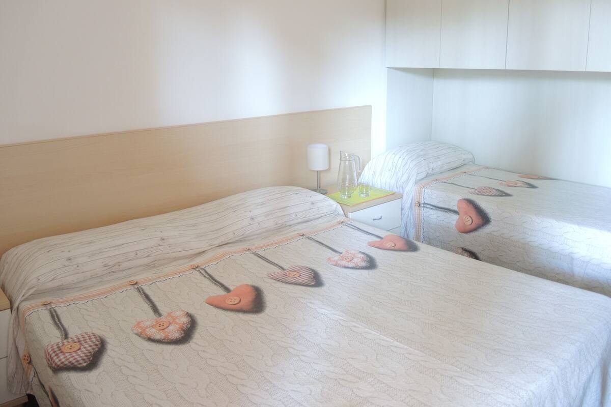 Deux lits simples avec des oreillers en forme de cœur, une table de chevet avec une lampe et un mur sobre.