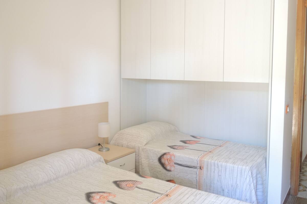 Une chambre avec deux lits simples, une table de chevet avec une lampe et une armoire.