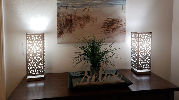 Un mur orné d’un tableau représentant une plage, deux luminaires décoratifs et une petite plante avec une pancarte indiquant « Détendez-vous ».