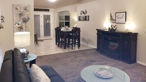 Un salon comprenant un canapé, une table basse, une cheminée et un coin repas avec une table dressée pour quatre personnes.